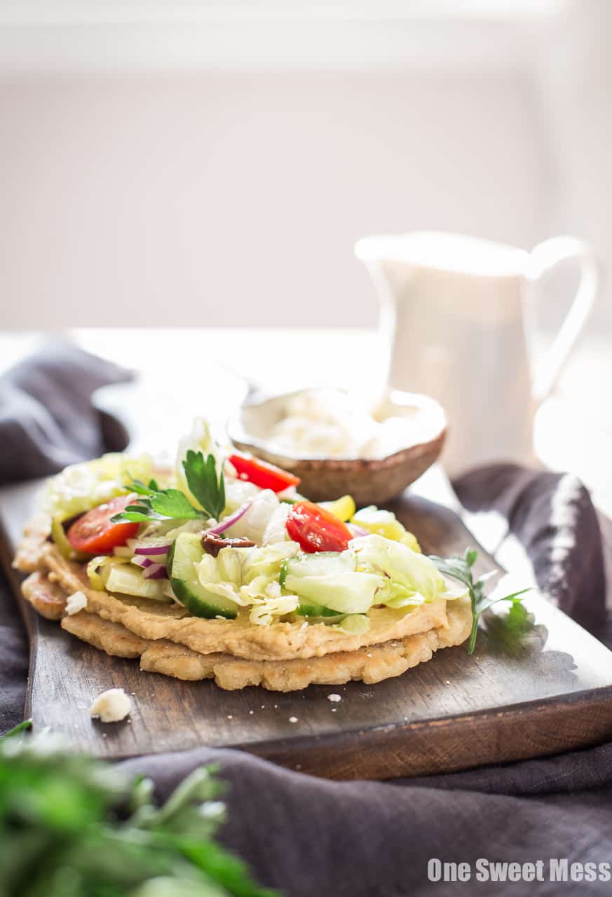 Gluten-Free Greek Salad Naan Pizza: Gluten-Free Naan smeared with creamy hummus and topped with a mound of fresh Greek salad.